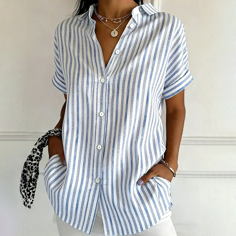 Woman in striped top, heart necklace, white pants.